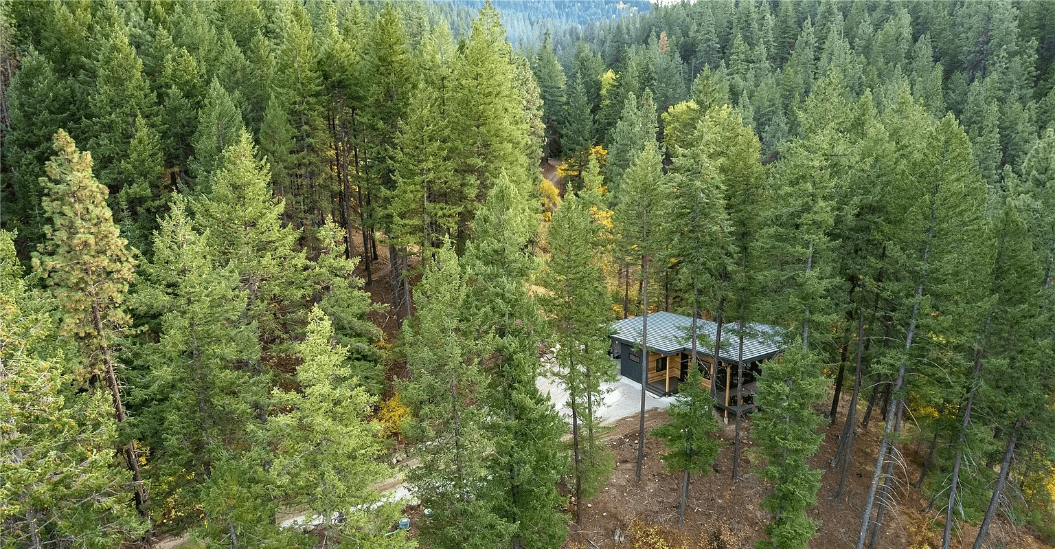 Aerial view of a modern, newly constructed single story home within a forested, mountainous area