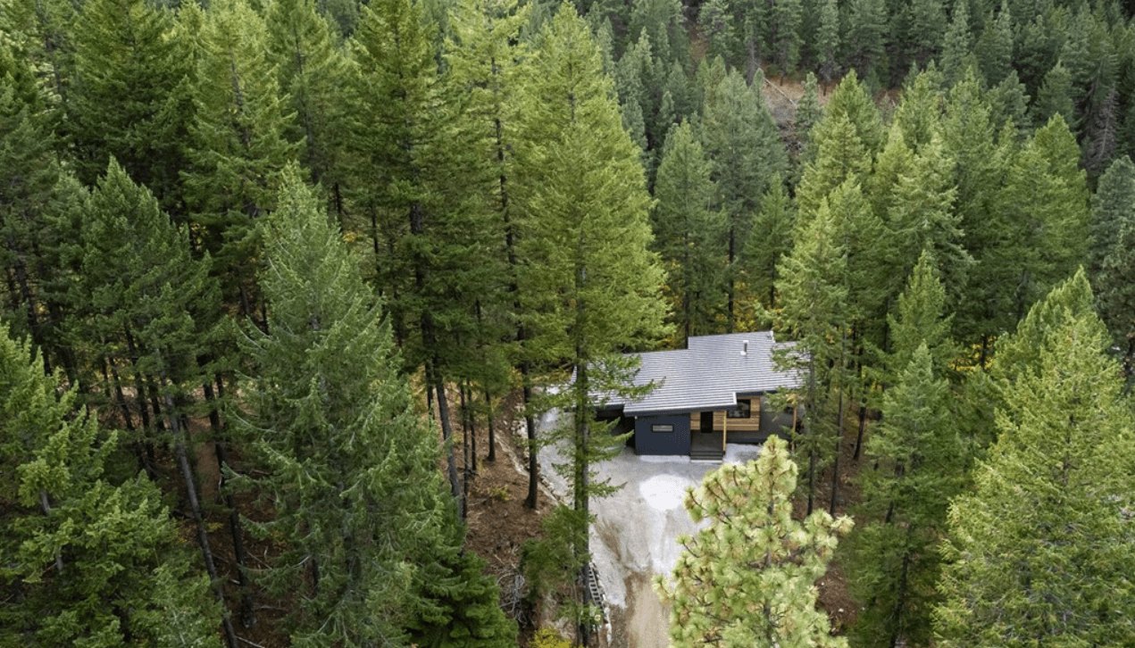 Aerial view of a modern, newly constructed single story home within a forested, mountainous area
