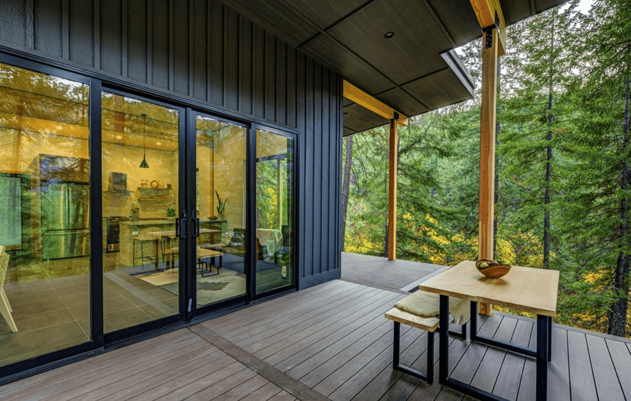 Close up of back deck of newly constructed home in forested area. Shows living area through large glass doors