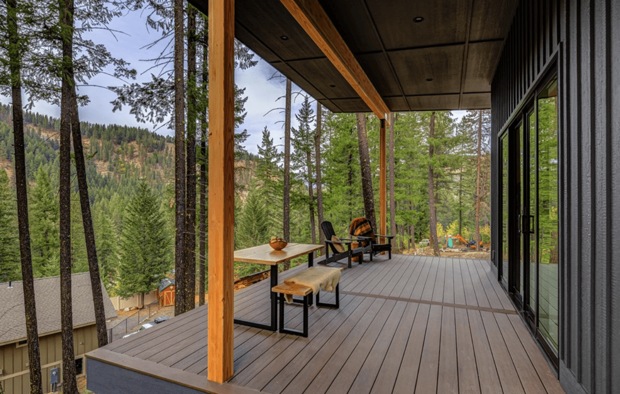 Back deck of newly constructed home with table, bench and chairs showcasing a forested overlook