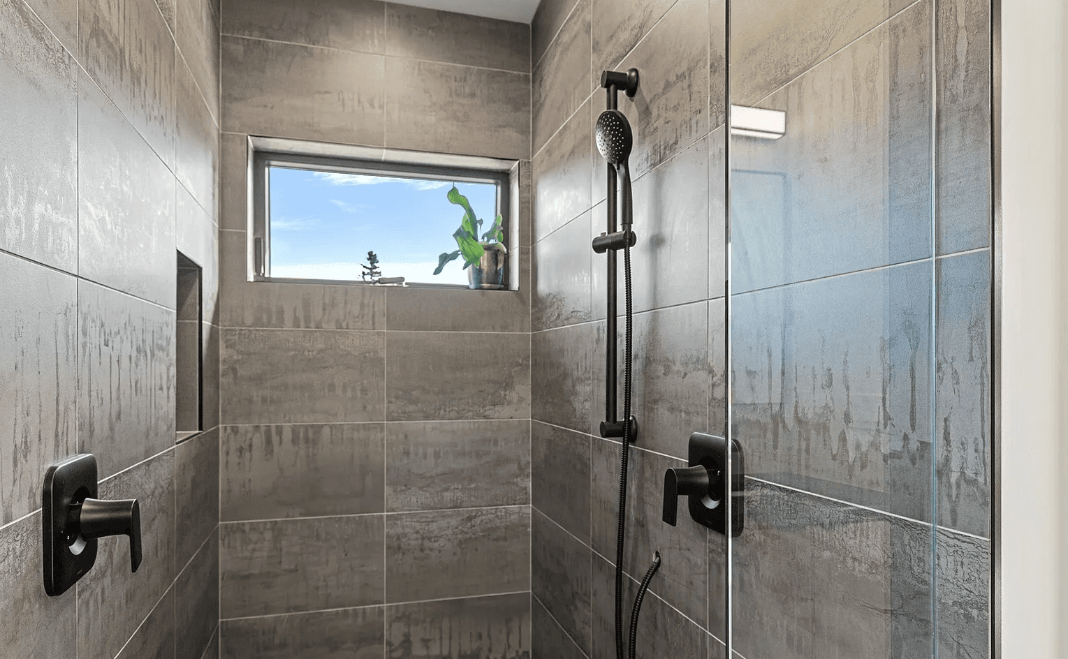 Modern, newly constructed shower with fully tiled walls, exterior window and black fixtures