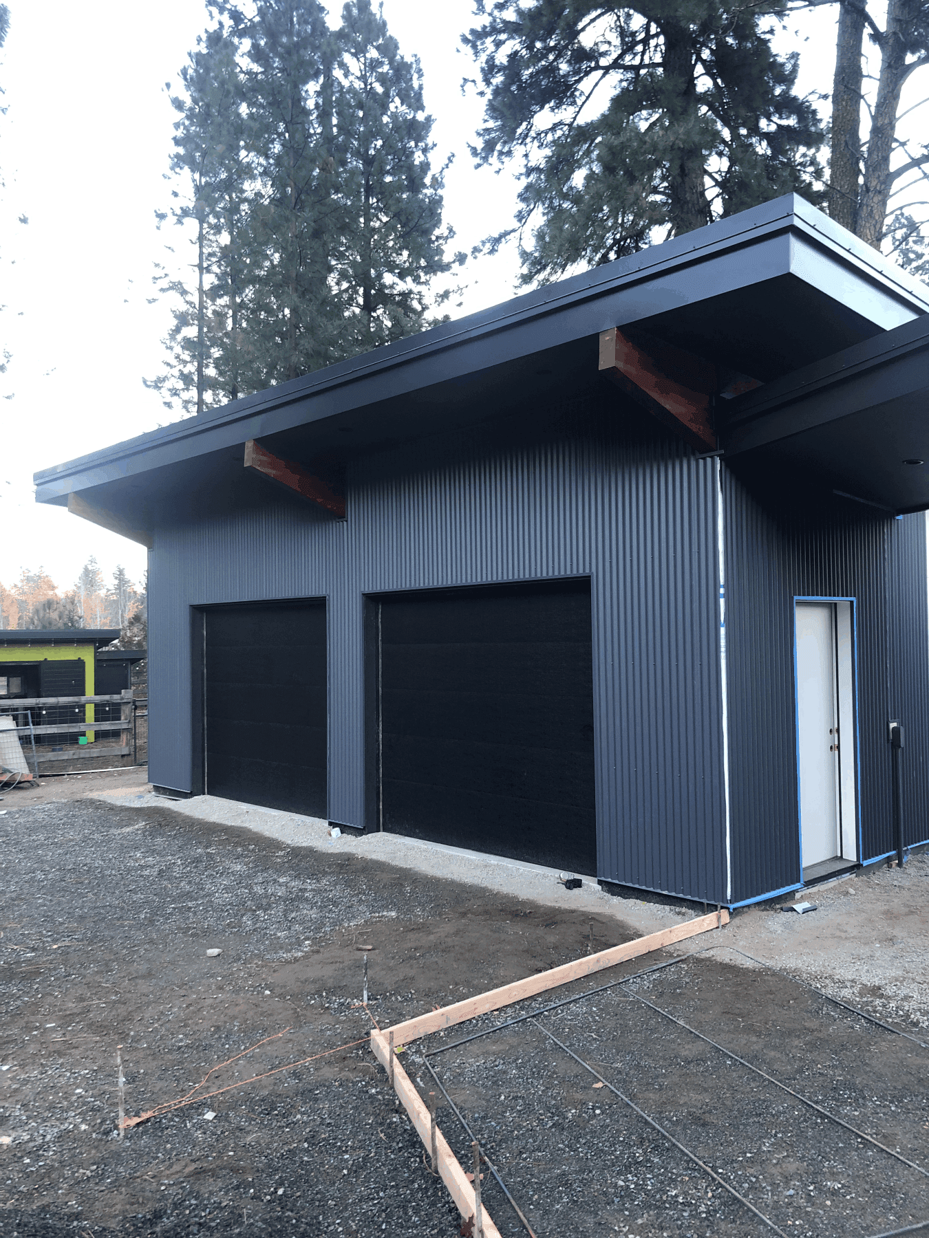 Graded dirt and excavator in foreground, newly constructed rear of garage in background