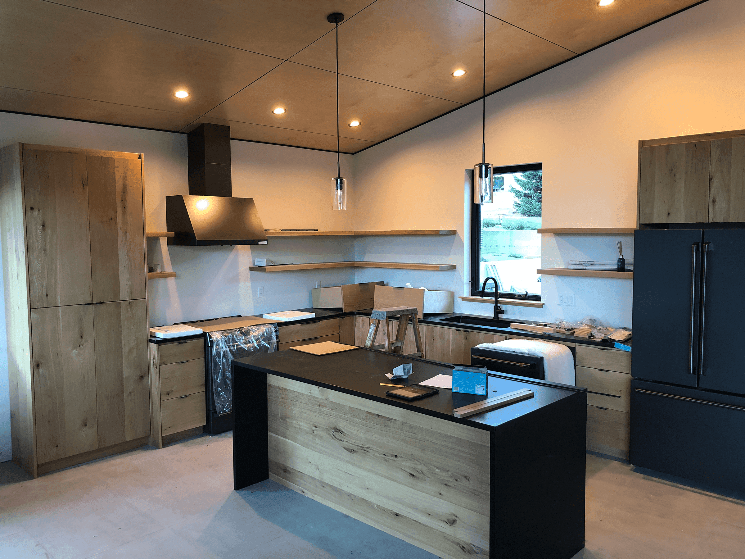 Interior of modern open plan kitchen under construction with custom cabinets, black appliances and countertops
