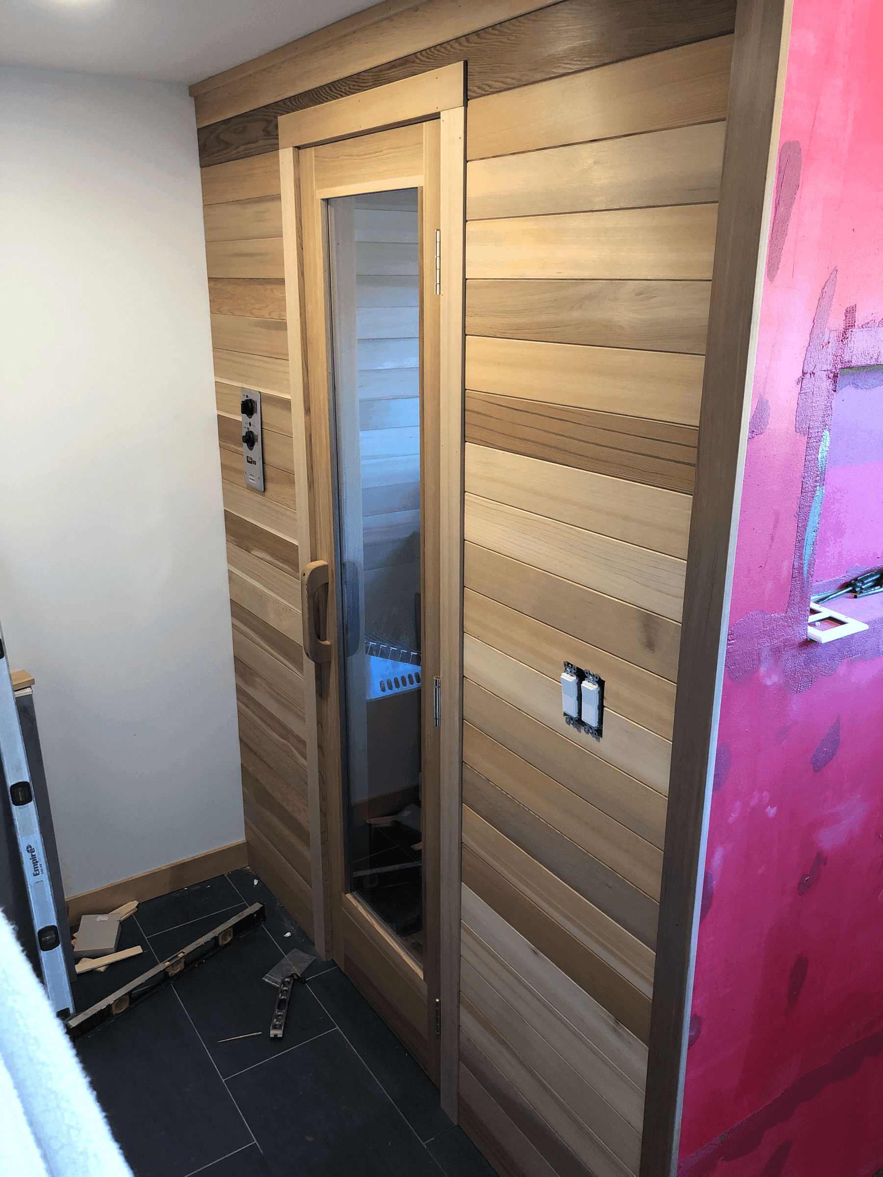 Close up of entrance to unfinished internal sauna with cedar wood paneling and adjacent shower
