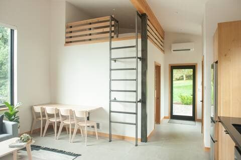 Interior of modern accessory dwelling unit showing steel ladder up to storage loft above table with four chairs