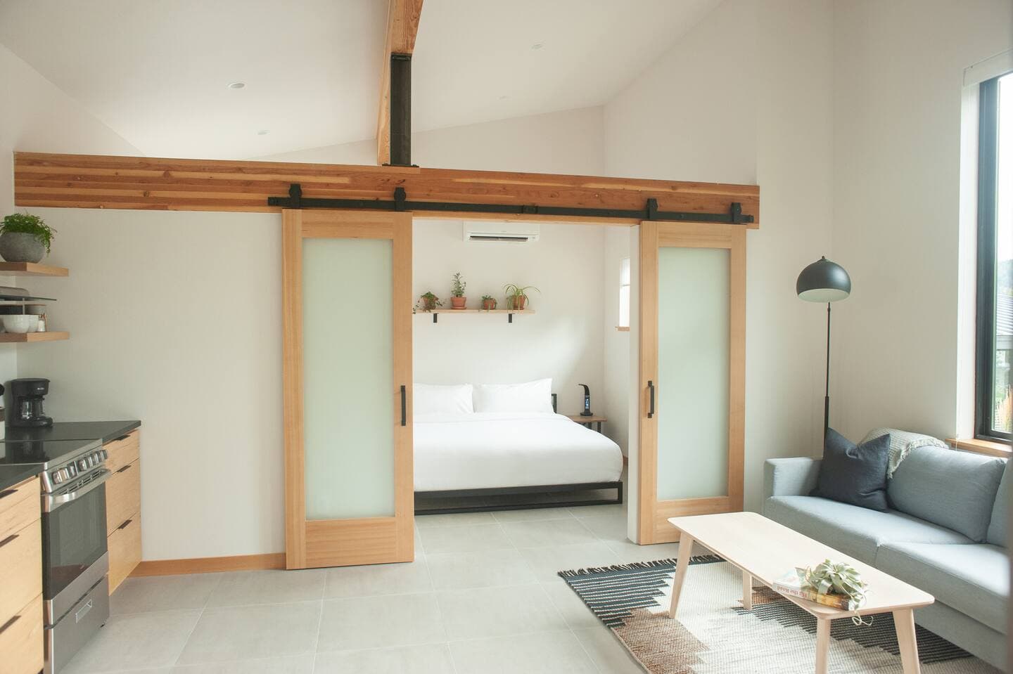 Interior of modern accessory dwelling unit showing open plan living area with couch and coffee table, with open sliding doors revealing bedroom with large bed