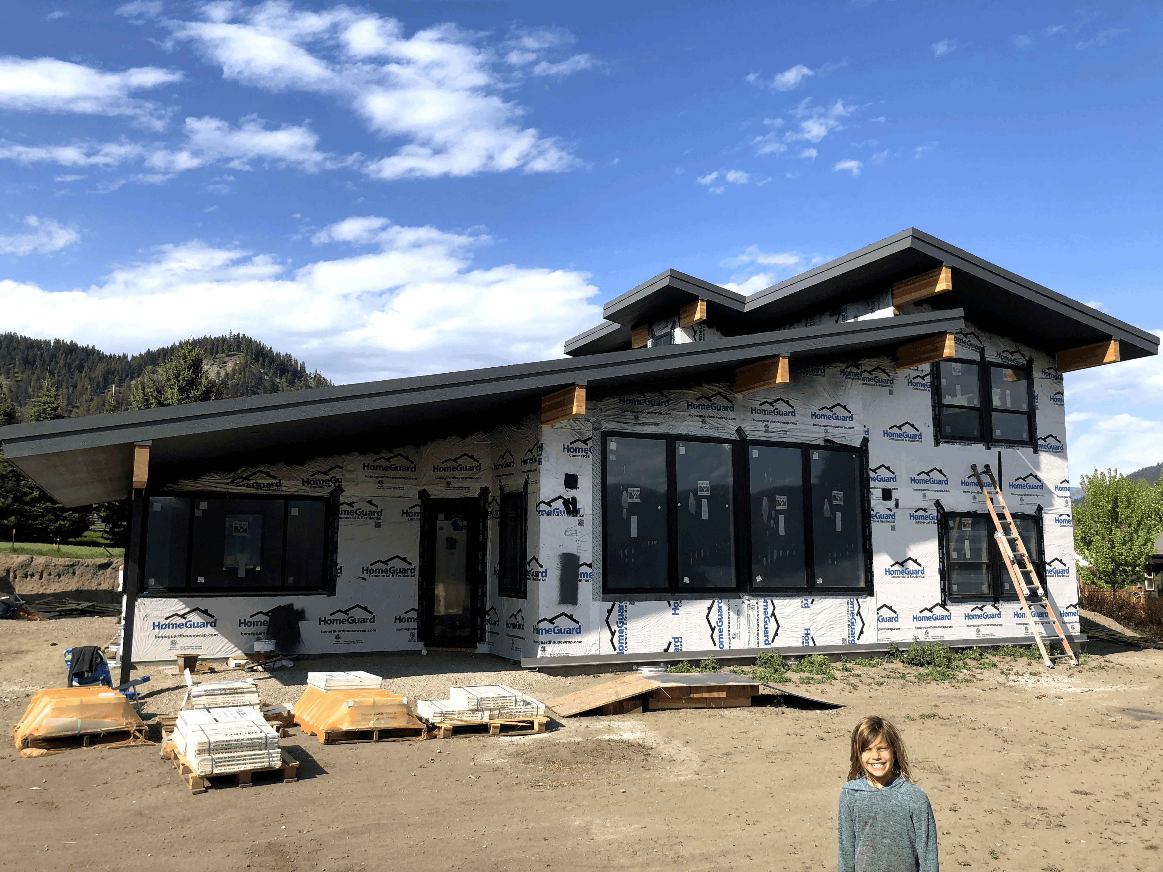 Front profile of modern two-story house with large windows and wooden accents prior to siding and exterior finishes